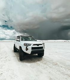 a white four - door suv parked in the middle of a snowy field under a cloudy sky