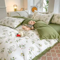 a teddy bear sitting on top of a bed with green sheets and pillows in a bedroom