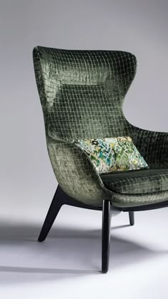 an upholstered green chair with a pillow on it's back and legs