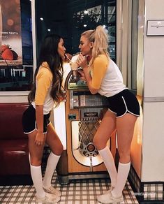 two women in short shorts and knee high socks standing next to each other near a vending machine