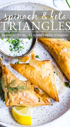 spinach and feta triangles on a white plate with lemon wedges, yogurt and dill