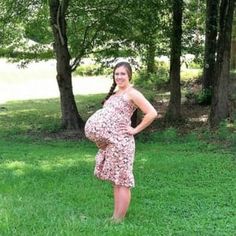 a pregnant woman standing in the grass with her hands on her hips