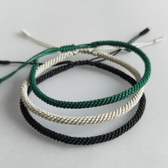 three different colored bracelets with black, white and green cords