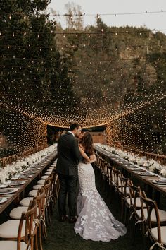 a bride and groom kissing in front of an outdoor dinner table set up with string lights