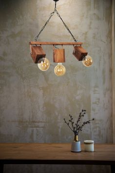 three lights hanging from a wooden beam on a wall next to a vase with flowers