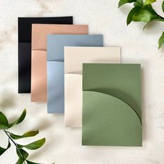 four different colored envelopes on a white surface with green leaves in the corner and one folded