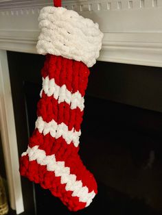 a red and white knitted christmas stocking hanging from a fireplace