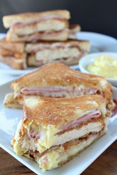 two halves of a ham and cheese sandwich on a white plate with dipping sauces