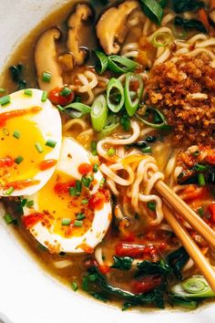 a bowl filled with noodles, meat and vegetables next to an egg on top of some chopsticks