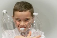 a young boy holding two empty water bottles in front of his face and making the peace sign