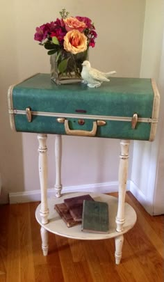 an old suitcase is sitting on a small table with flowers in the vase and books