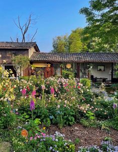 a house with lots of flowers in front of it and trees around the back yard