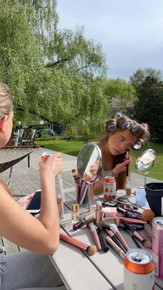 two women sitting at a picnic table with makeup and other items on top of it