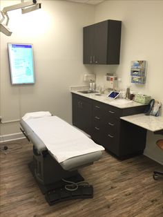 a medical room with an exam table in the middle and a monitor on the wall