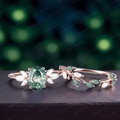 two rings with green and white stones on them sitting on top of a wooden table