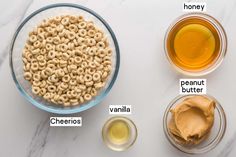 ingredients to make peanut butter cheerios in bowls on a white marble counter top with honey, peanut butter and peanuts