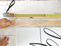 a person holding a pencil next to a piece of wood with a tape measure on it