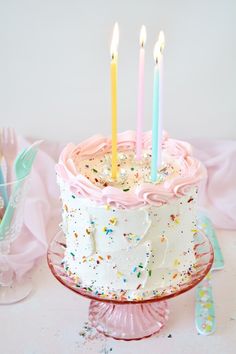 a birthday cake with white frosting and pink icing has five lit candles on it