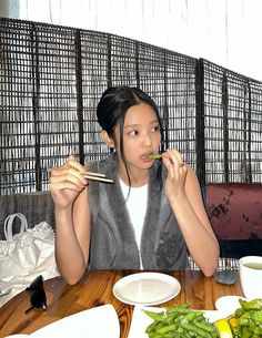 a woman sitting at a table with chopsticks in her mouth while eating green beans