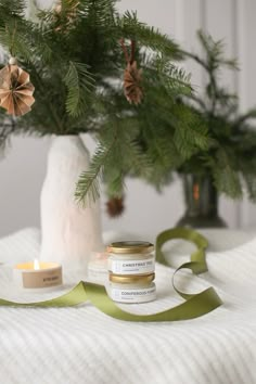 a candle and some green ribbon on a bed next to a christmas tree with pine cones