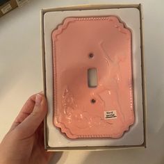 a pink light switch cover in a box with a hand holding it up to the camera