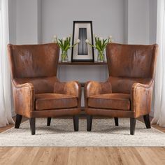 two brown leather chairs sitting next to each other on top of a hard wood floor