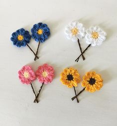 four crocheted flowers are arranged on a white surface, one is yellow, the other is blue