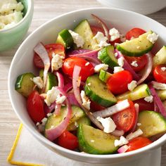 a white bowl filled with cucumber, tomatoes and onions next to a green bowl full of feta cheese