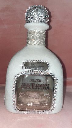 a white bottle with a silver crown on it's top sitting on a pink surface