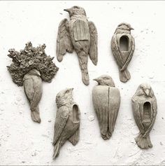 six bird sculptures are displayed on a white wall and one is made out of clay