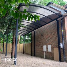 an open carport in front of a brick building with trees and bushes around it