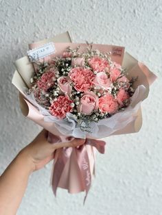 a person holding a bouquet of pink carnations with baby's breath in it