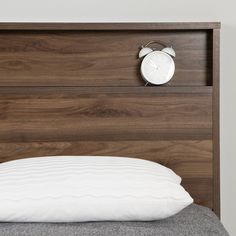 an alarm clock on the side of a wooden headboard next to a white pillow