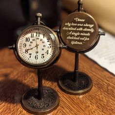 two small clocks sitting next to each other on a wooden table with writing on them