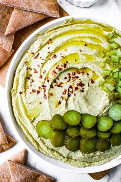 a white bowl filled with hummus, pickles and crackers