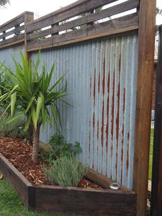 a wooden planter filled with plants next to a metal fence and grass covered ground