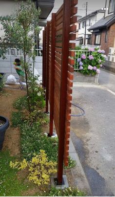 a person is watering water from a hose in a yard with plants and flowers on the side