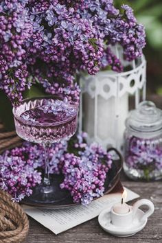 purple flowers are sitting on a table next to a cup and saucer with a candle