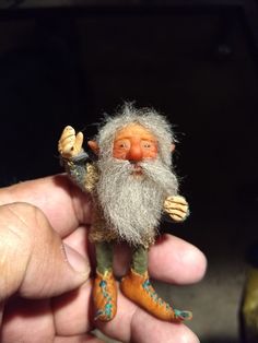 a hand holding a small toy with a white beard and long gray hair on it