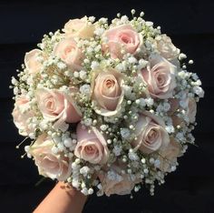 a bouquet of pink roses and baby's breath is being held by a hand