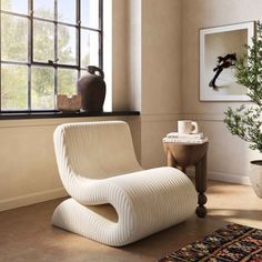 a white chair sitting in front of a window next to a potted green plant