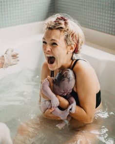 a woman holding a baby in a bathtub with her mouth open and tongue out