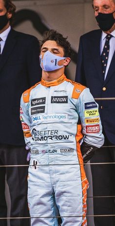 a man in a race suit and face mask standing next to other men wearing suits