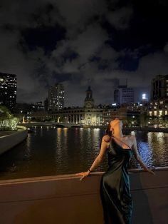 a woman is standing on the edge of a bridge looking at the water and buildings