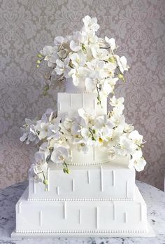 a three tiered white wedding cake with flowers on the top and bottom, sitting on a marble table