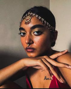 a woman in a red dress with gold jewelry on her head and hand near her face