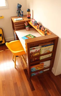 a wooden desk topped with lots of books and toy figurines next to a yellow chair