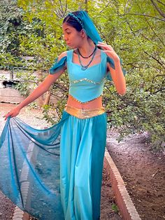 a woman in a blue belly dance outfit and headpiece is standing on a bridge