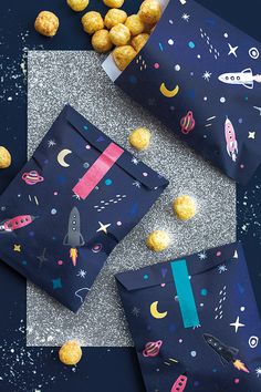 two bags with space themed wrapping paper on them and some snacks in the background that include macaroni and cheese