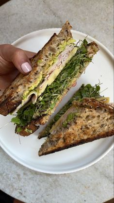 a person holding a sandwich on top of a white plate